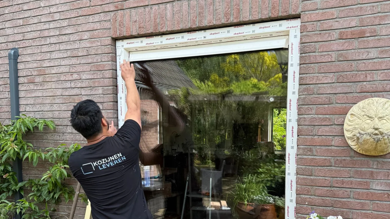Medewerker controleert een kunststof kozijn in een gemetselde gevel